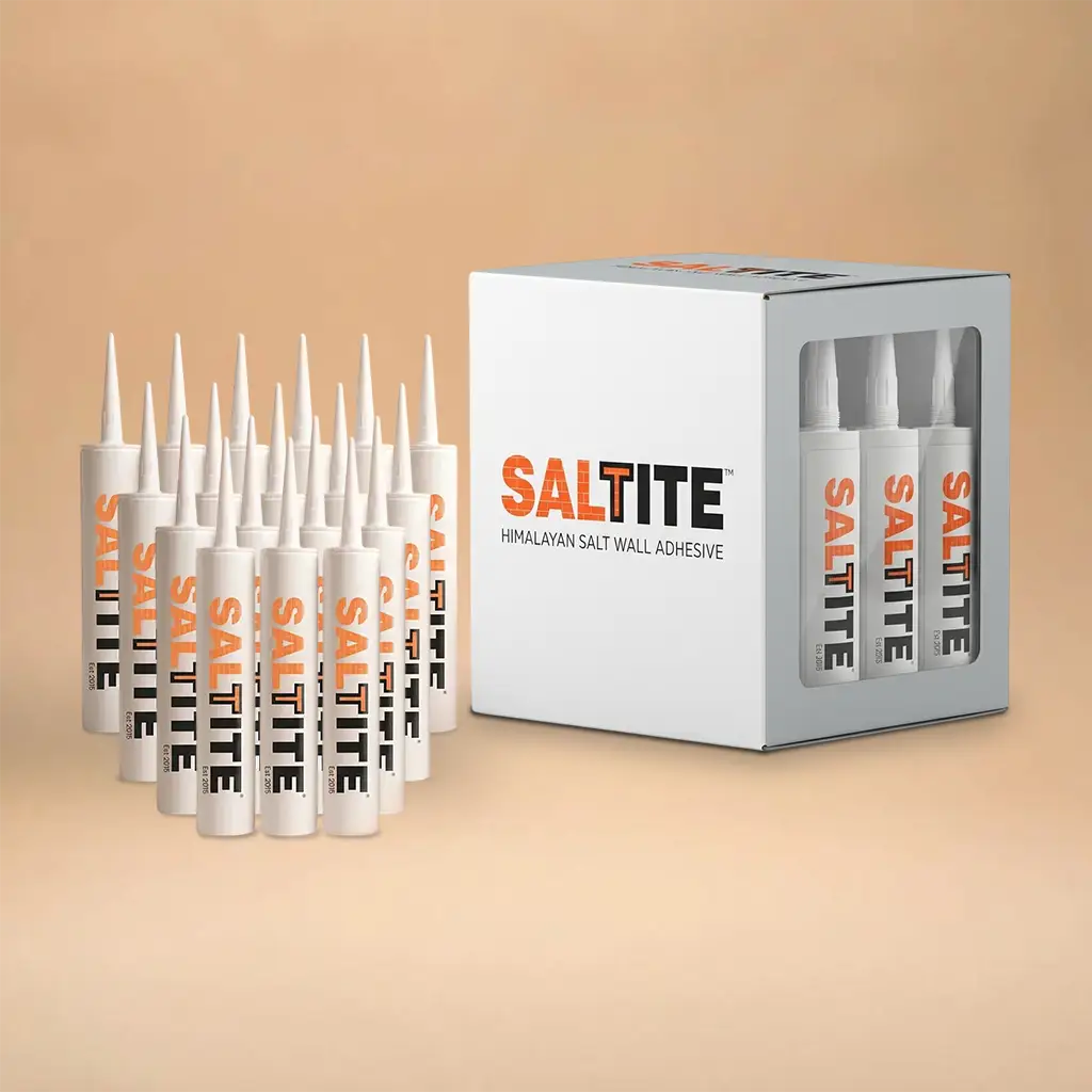A box of SALTITE Himalayan salt wall adhesive next to several white squeeze tubes with orange and black branding, arranged on a warm beige background.